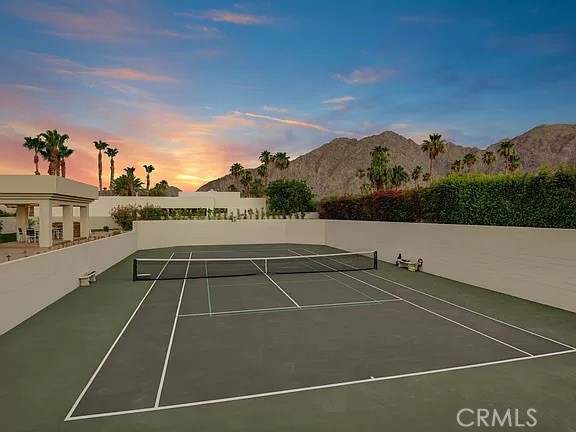 Outdoor tennis court with mountain views and palm trees at sunset.