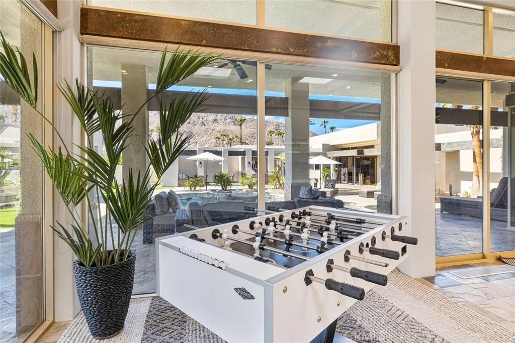 Game room with a white foosball table and potted palm, looking out to the pool patio.