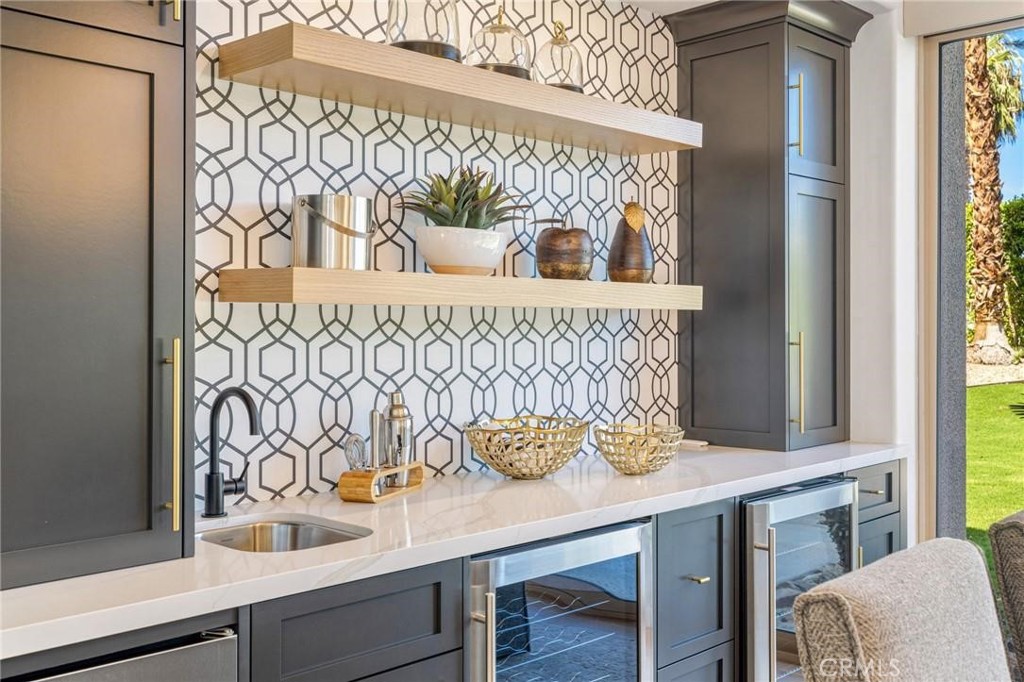 Built-in wet bar with geometric tile backsplash, floating wood shelves, small sink, and beverage refrigerators.