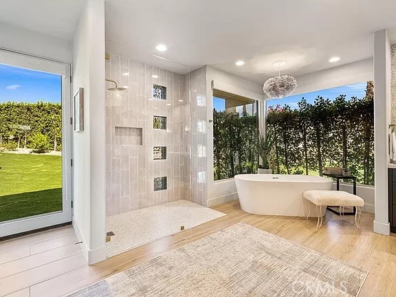 Bright bathroom with a walk-in shower and freestanding tub beside large garden-facing windows.