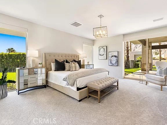 Furnished bedroom with a tufted bed, cushioned bench, and glass doors opening to a landscaped patio.