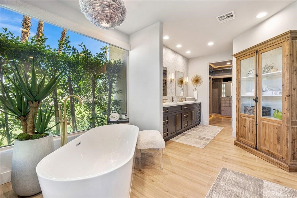 Bathroom with a freestanding tub beside a large window overlooking lush greenery.