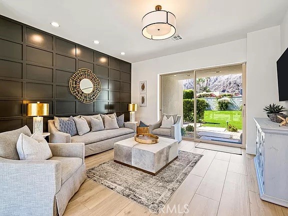 Staged living room with a light sectional, dark paneled accent wall, and sliding doors overlooking a lawn and pool.
