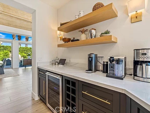 Beverage bar with floating wood shelves, coffee equipment, and dark cabinetry beside an open patio doorway.