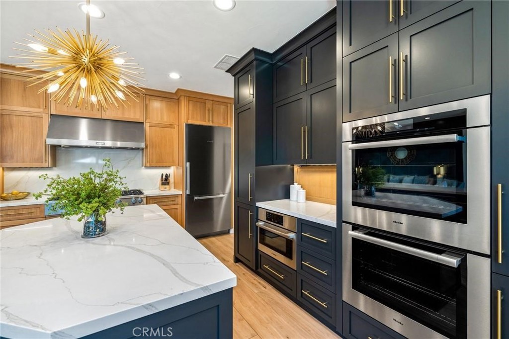 Modern kitchen with contrasting wood and navy cabinets, a veined island, and brass accents.