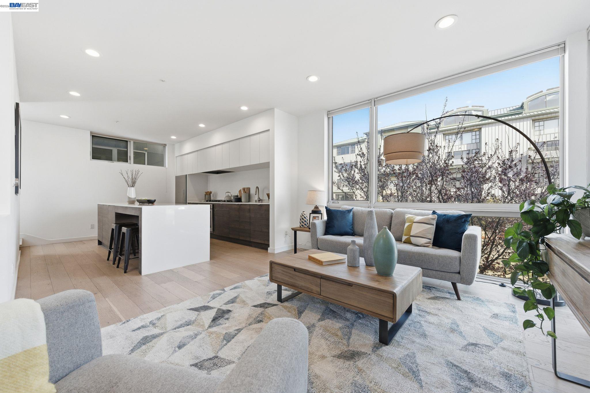 Open-plan living room and kitchen with large windows, a gray sofa, and a white island.