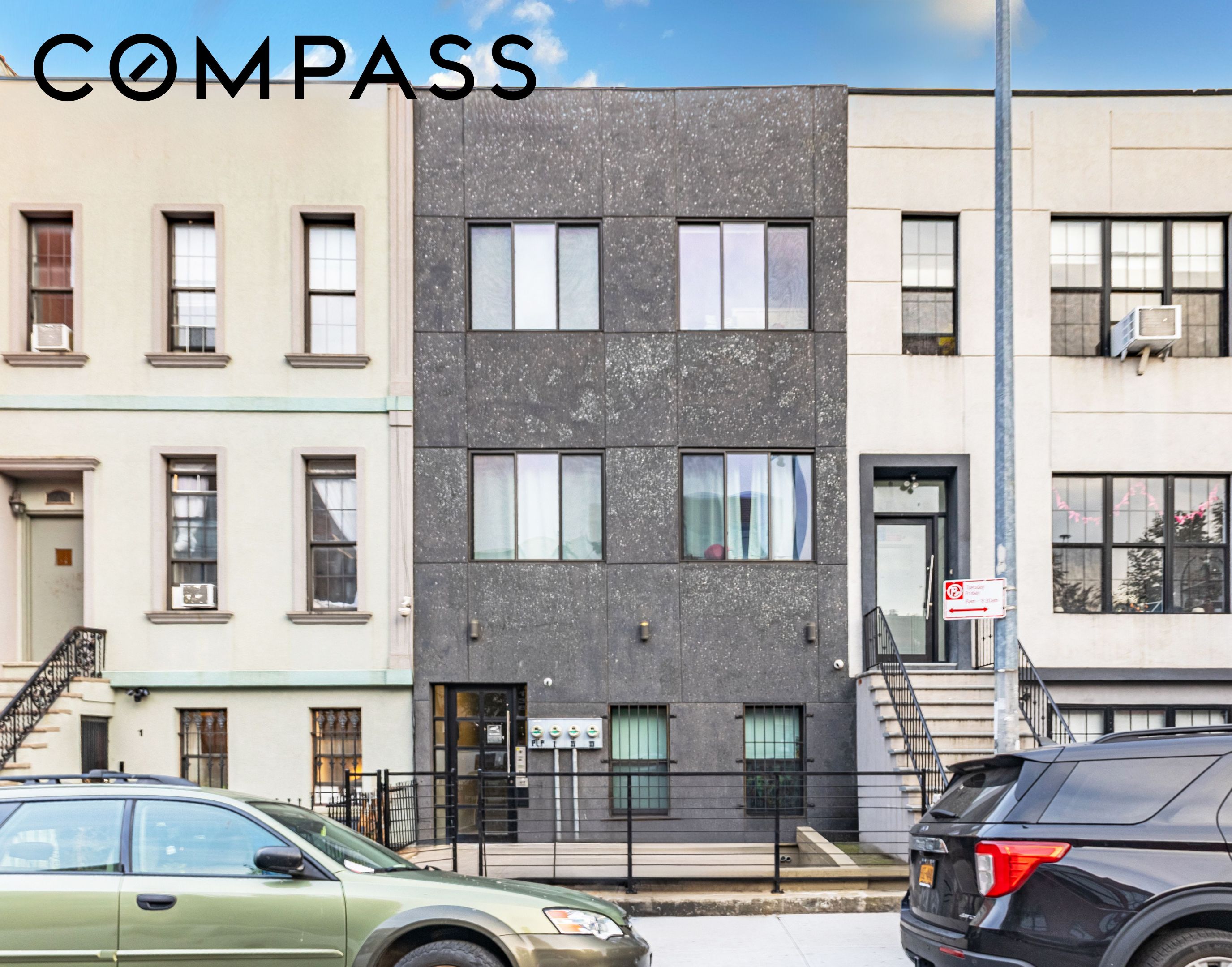 Modern dark-gray apartment building between cream-colored buildings, photographed from across the street.