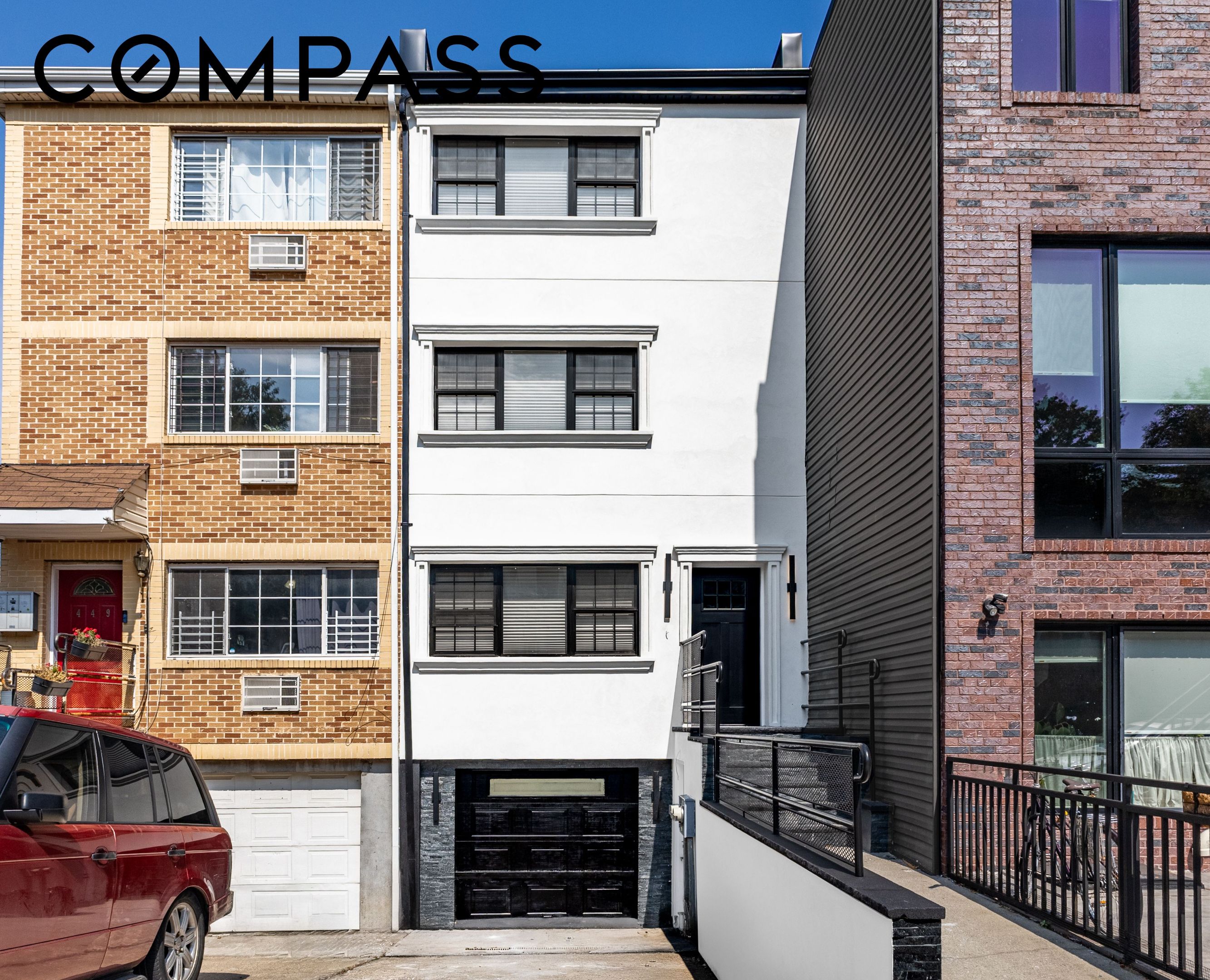 White townhouse with black garage and entry between brick neighboring buildings.