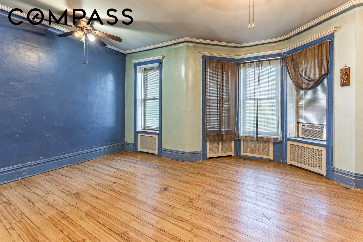Empty room with hardwood floors, blue and green walls, and bay windows with blinds.