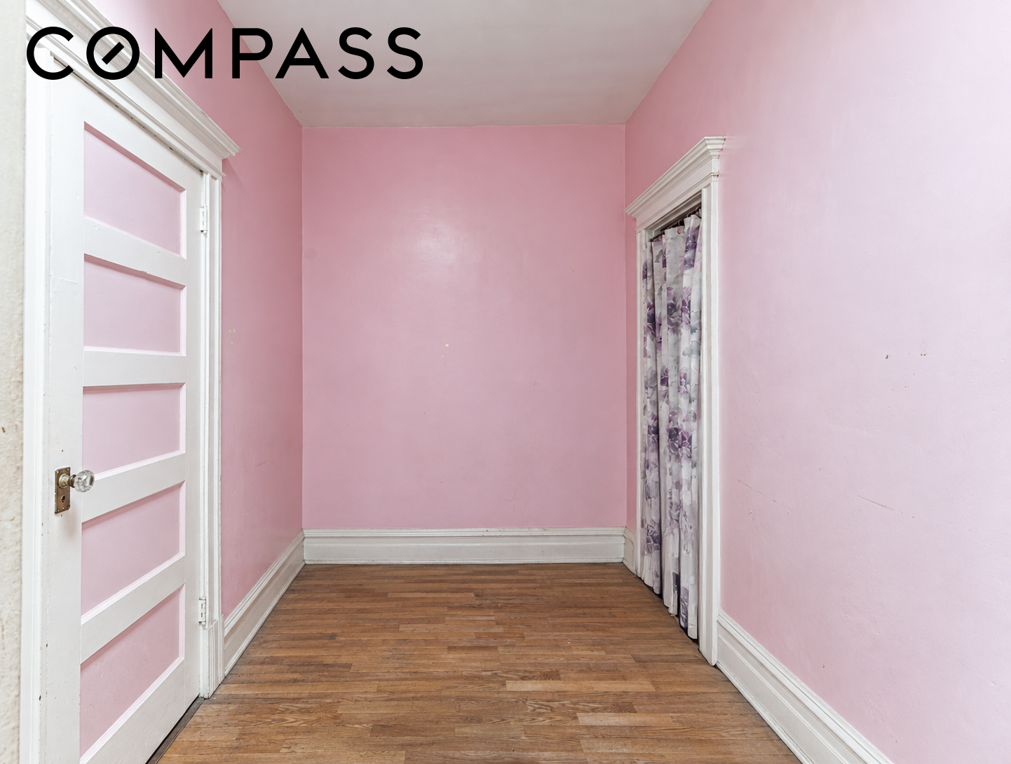 Empty pink room with hardwood floors, white trim, and a curtained doorway.