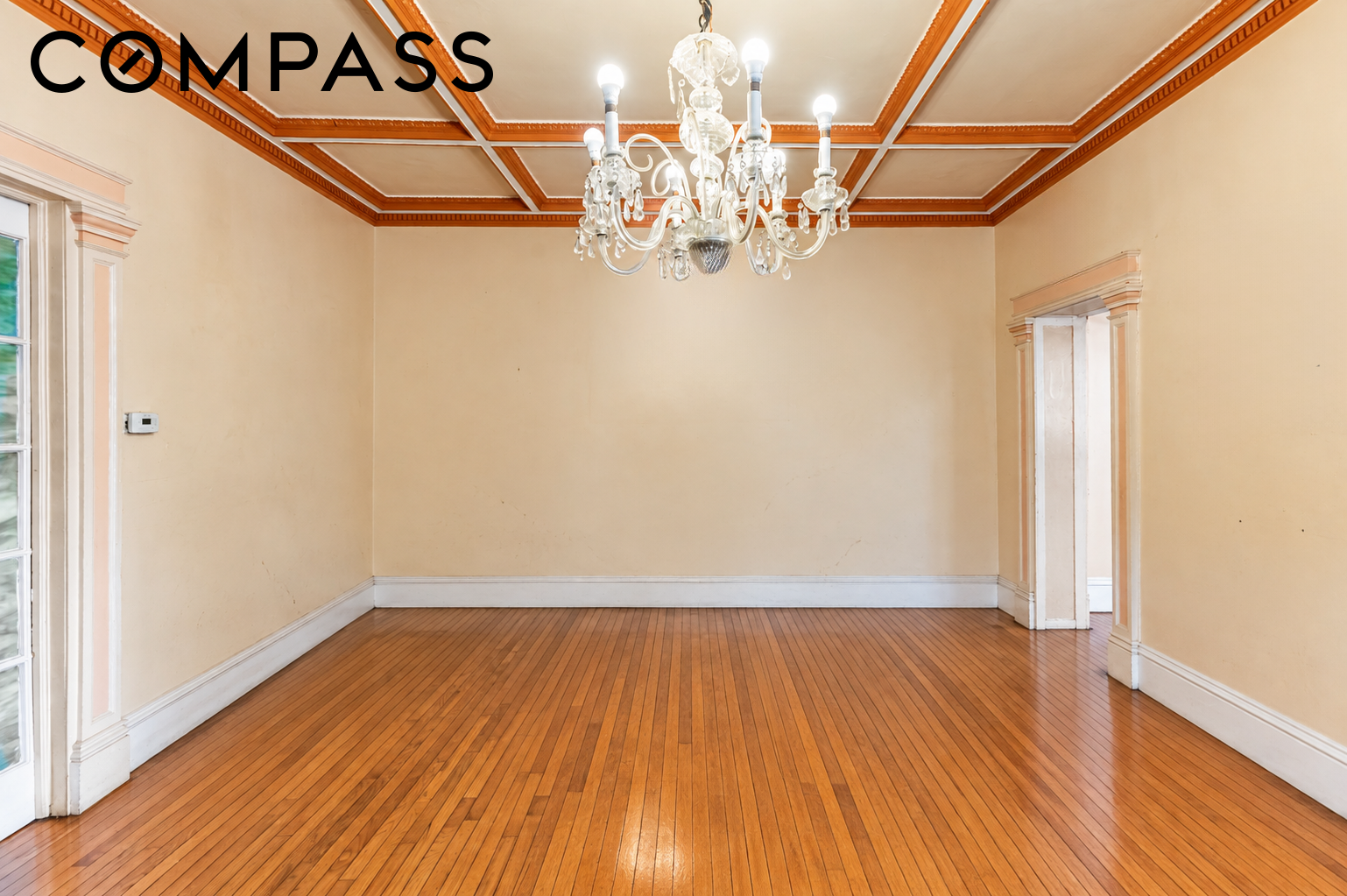 Empty dining room with polished hardwood floors, ornate coffered ceiling, and glass chandelier.