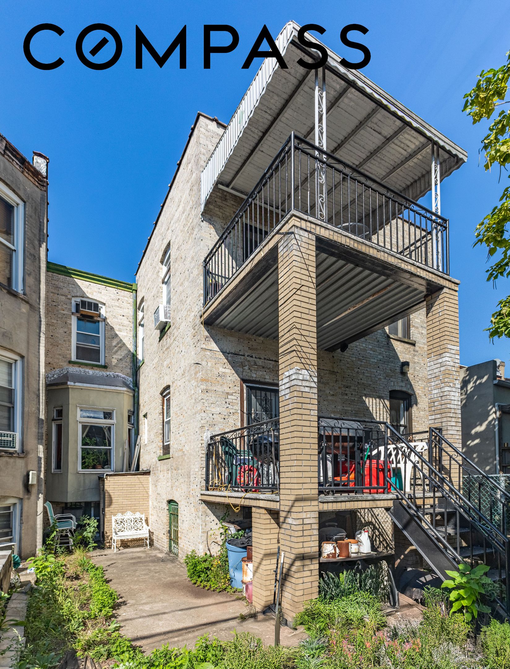 Brick residence rear exterior with stacked balconies, an outdoor staircase, and a small garden patio.