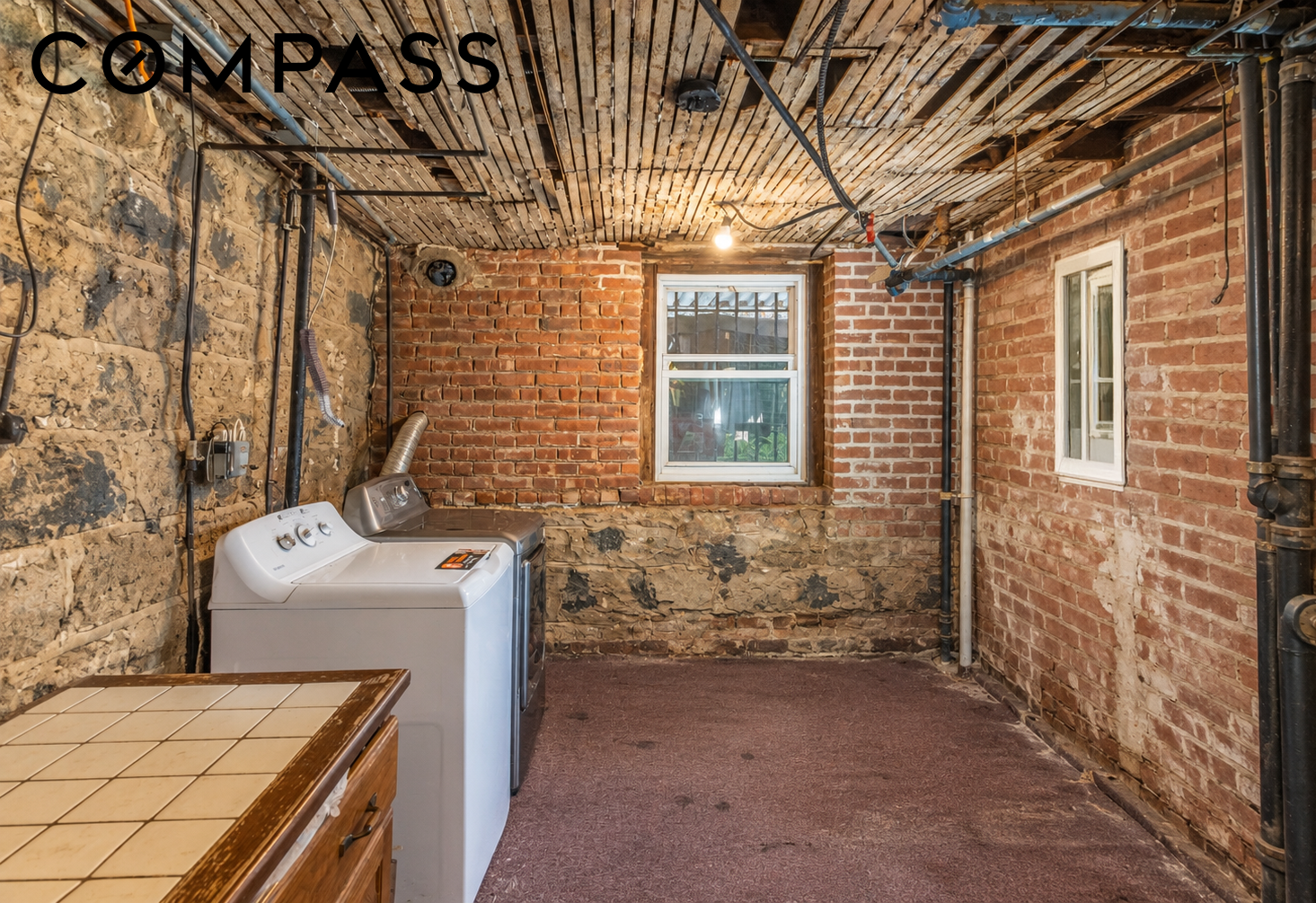 Basement laundry room with exposed brick walls, washer and dryer, and a wood-slat ceiling.