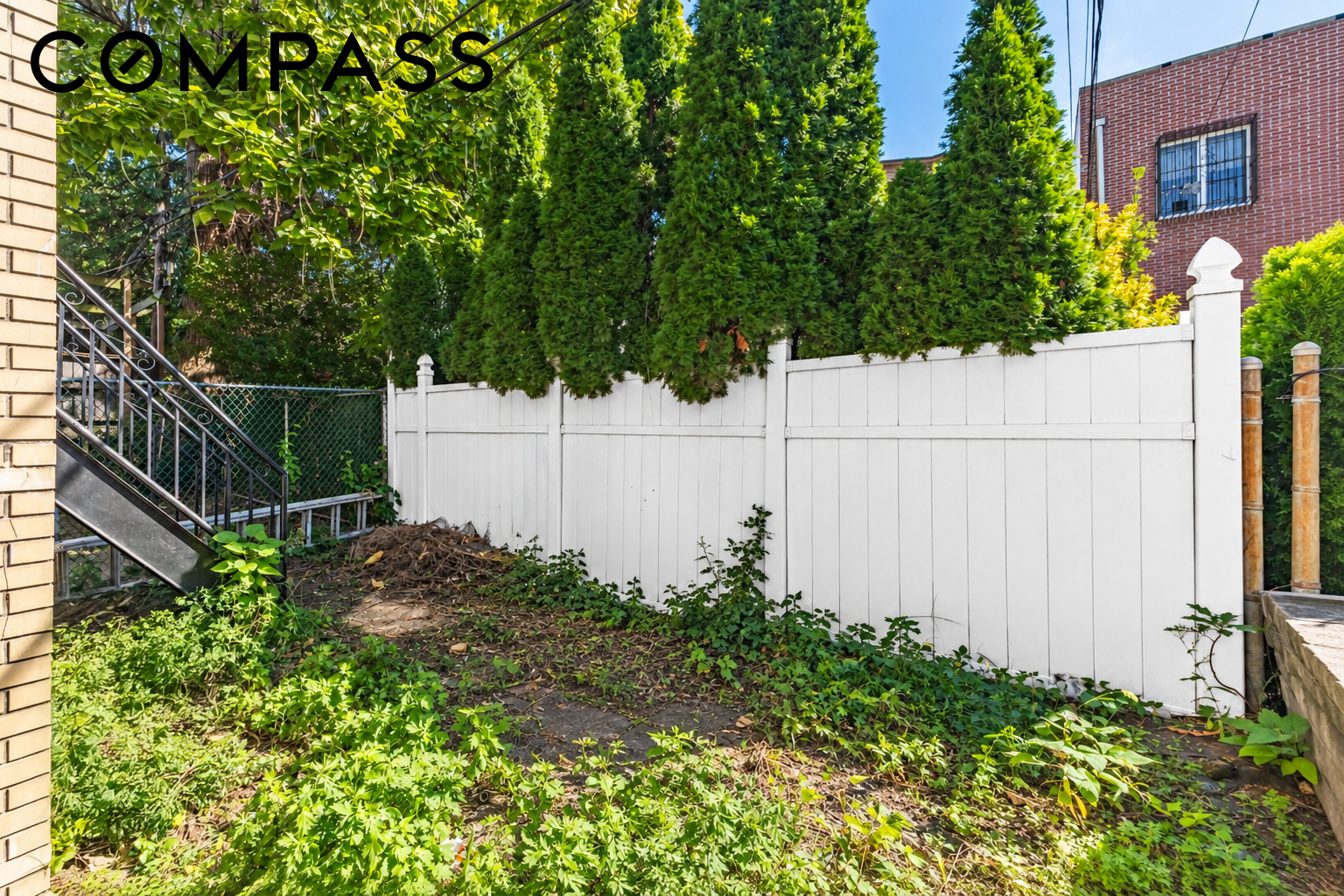 Backyard with a white privacy fence, dense greenery, and exterior stairs.
