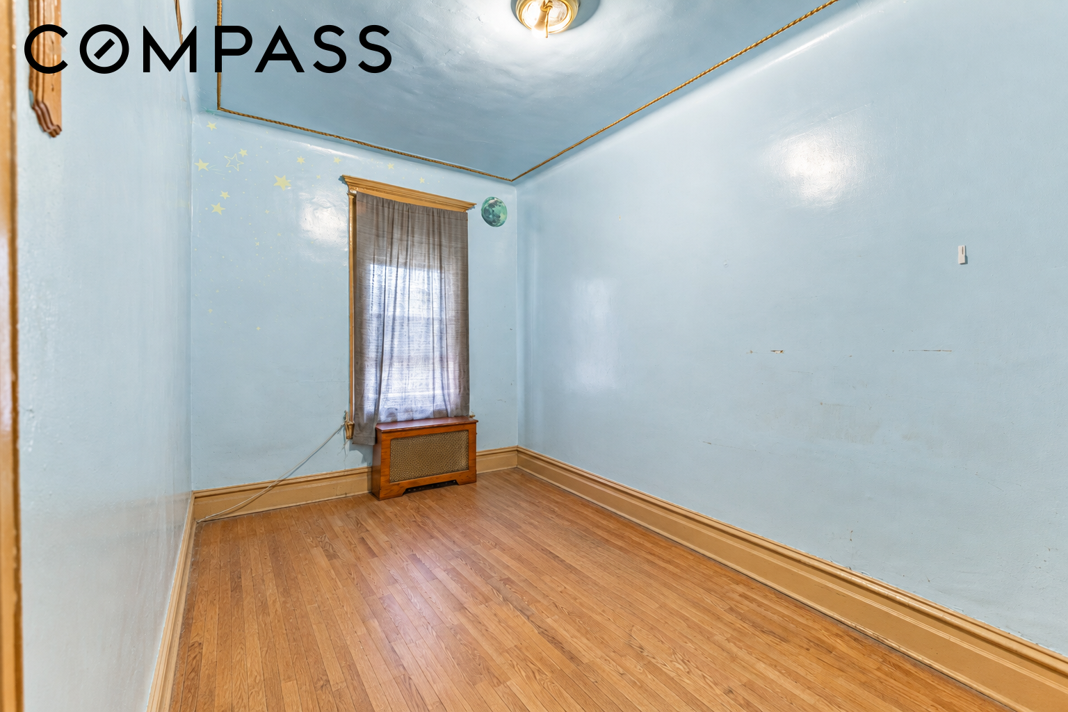 Empty blue room with star decals, a curtained window, wooden radiator cover, and hardwood floors.