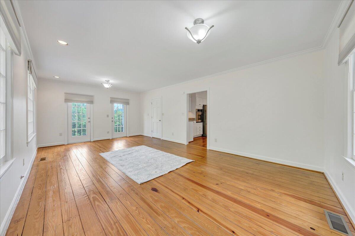 Bright, mostly vacant living room with hardwood floors, large windows, and glass-paneled doors.