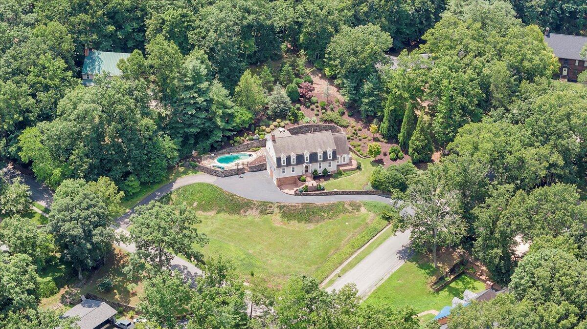 Aerial view of a home surrounded by trees, with a swimming pool and stone patio.