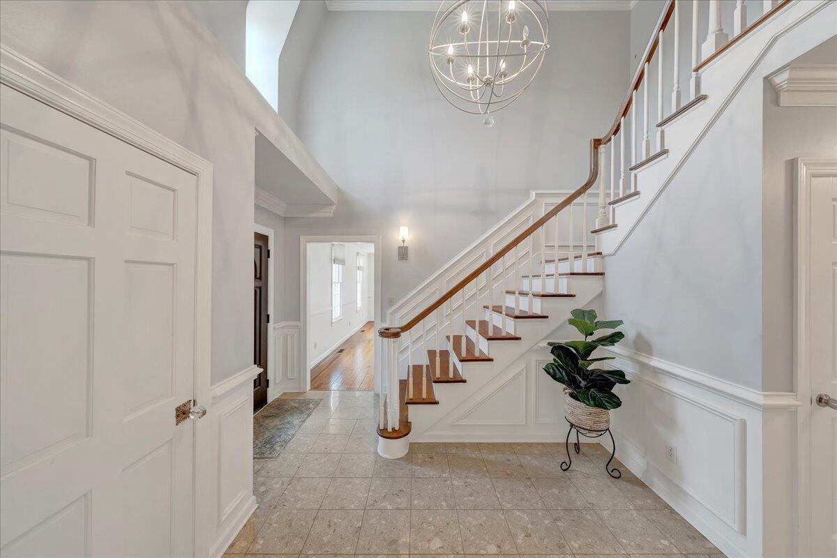 Two-story foyer with a sweeping staircase, spherical chandelier, pale tile floor, and potted plant.