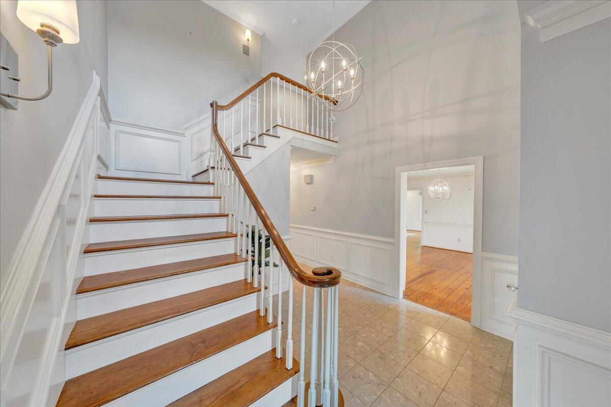 Foyer with a wood-and-white staircase, tiled floor, and spherical chandelier.