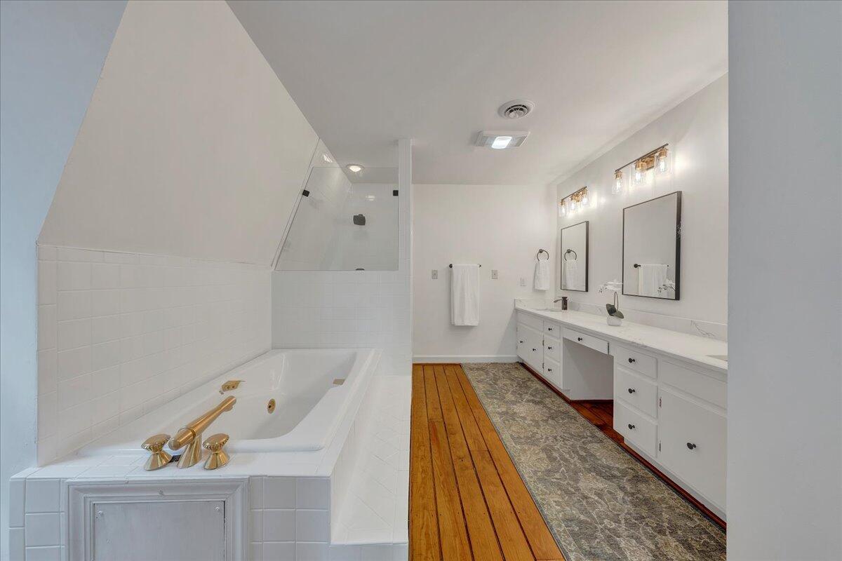 Bathroom with a built-in soaking tub, tiled shower, and long double vanity beside hardwood flooring.