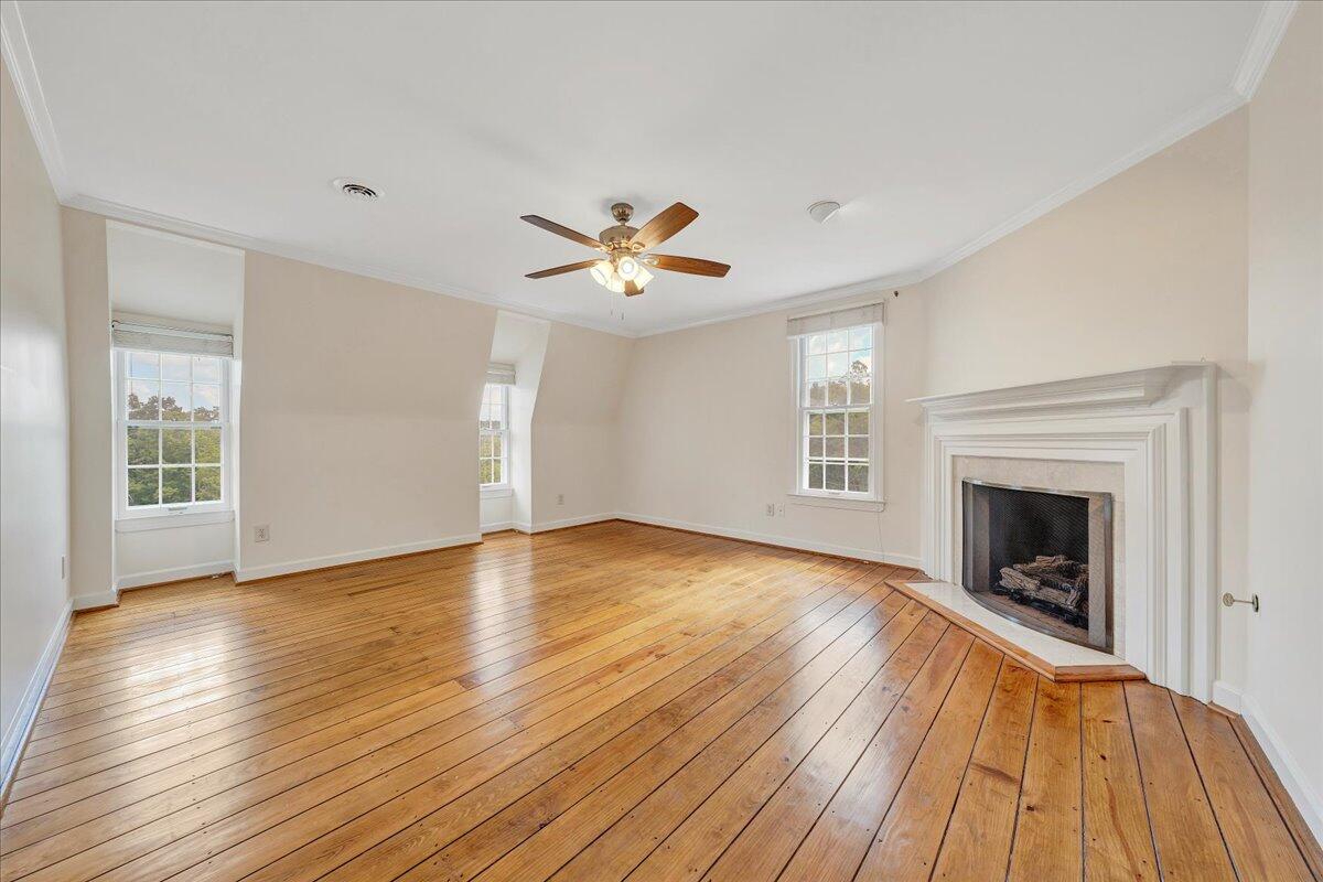 Empty living room with hardwood floors, a white fireplace, and three windows.