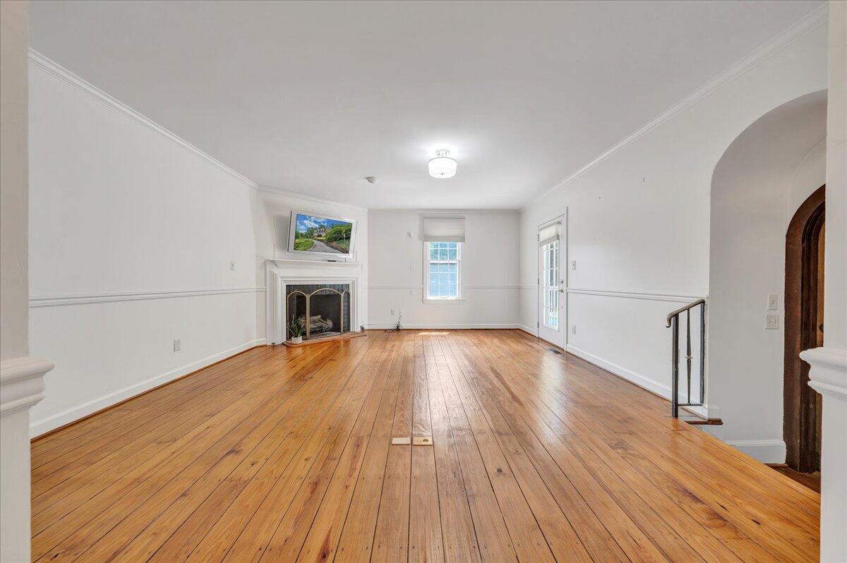 Empty living room with polished hardwood floors, a fireplace, and a television above the mantel.