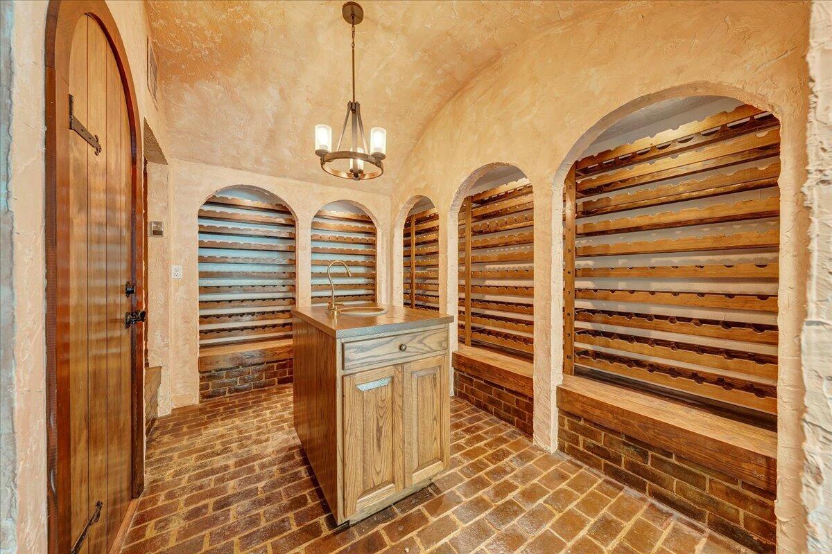 Wine cellar with arched wooden wine racks, a central sink island, and a brick floor.