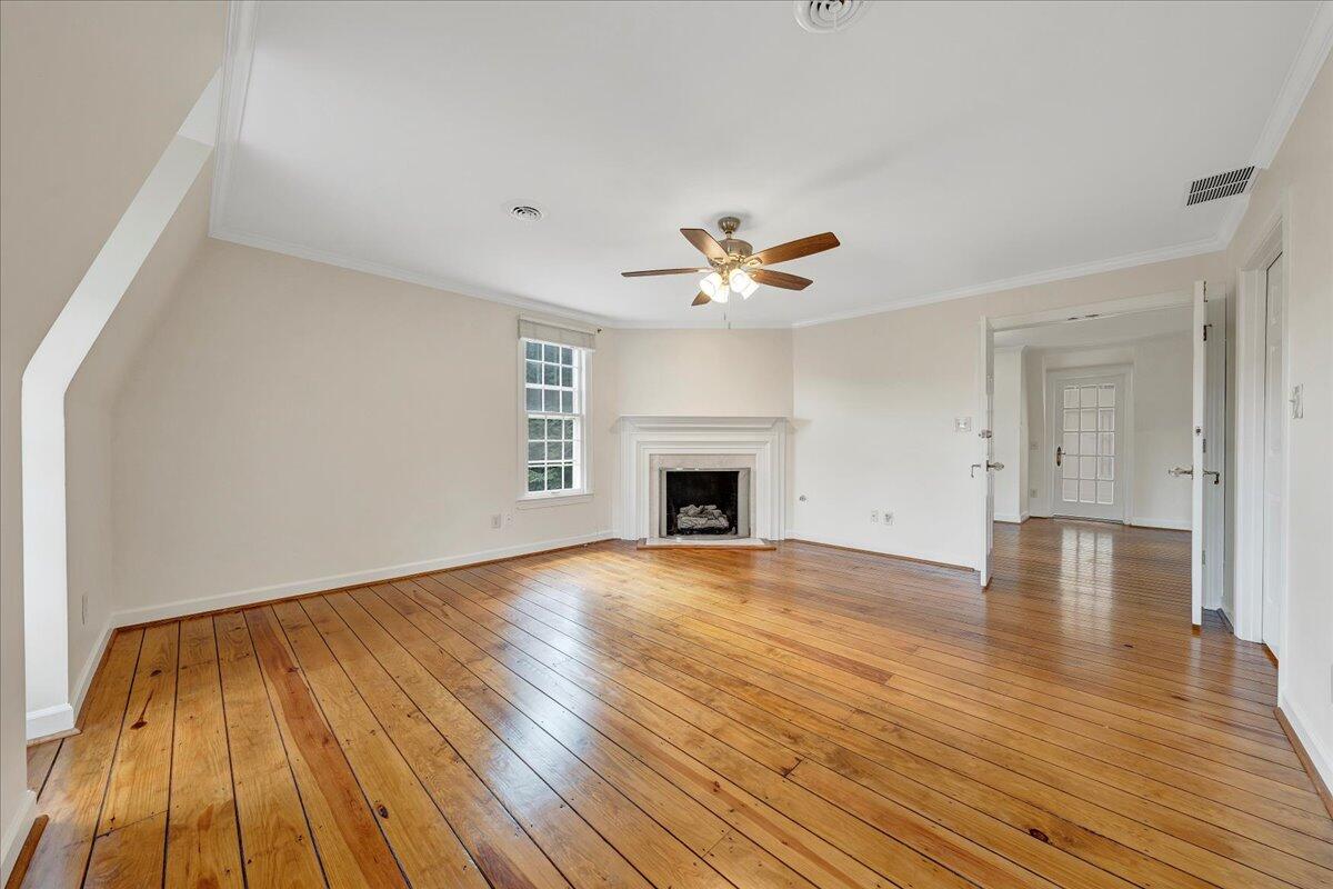 Empty living room with polished hardwood floors, a white fireplace, and a ceiling fan.