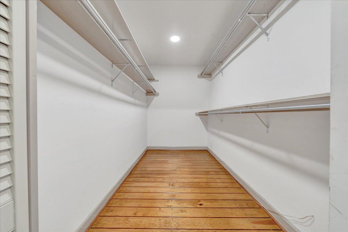 Empty walk-in closet with built-in hanging rods and shelves and a warm wood plank floor.