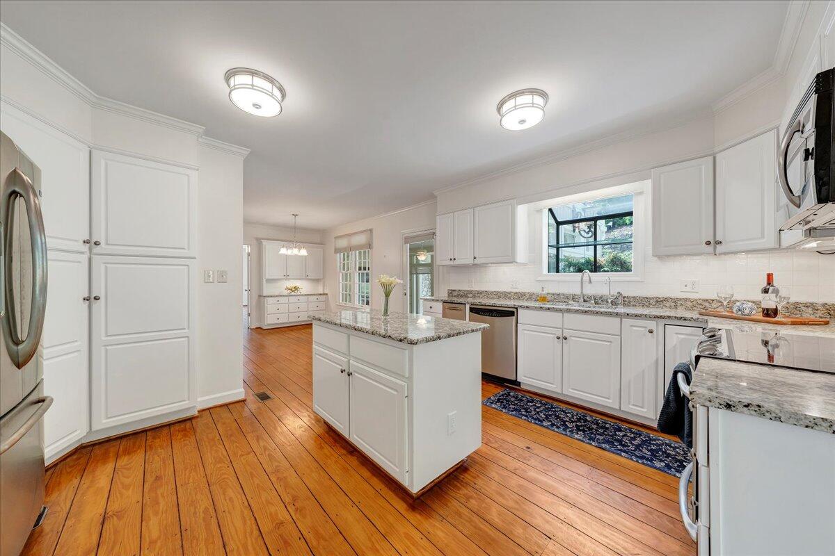 Bright kitchen with a granite-topped island, white cabinets, stainless appliances, and warm wood floors.
