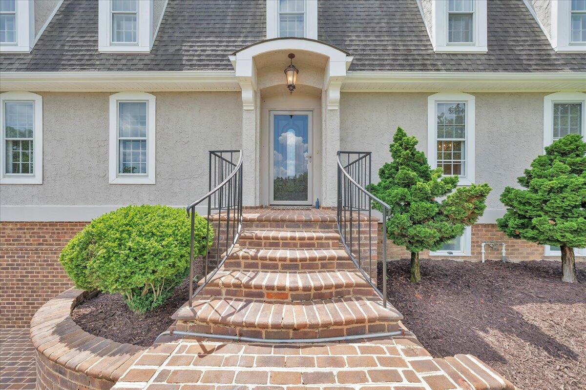 Home entrance with curved brick steps, an arched portico, and landscaped shrubs.