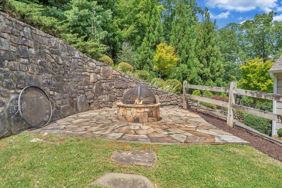 Stone patio with a round fire pit, tall retaining wall, and wooden fence.