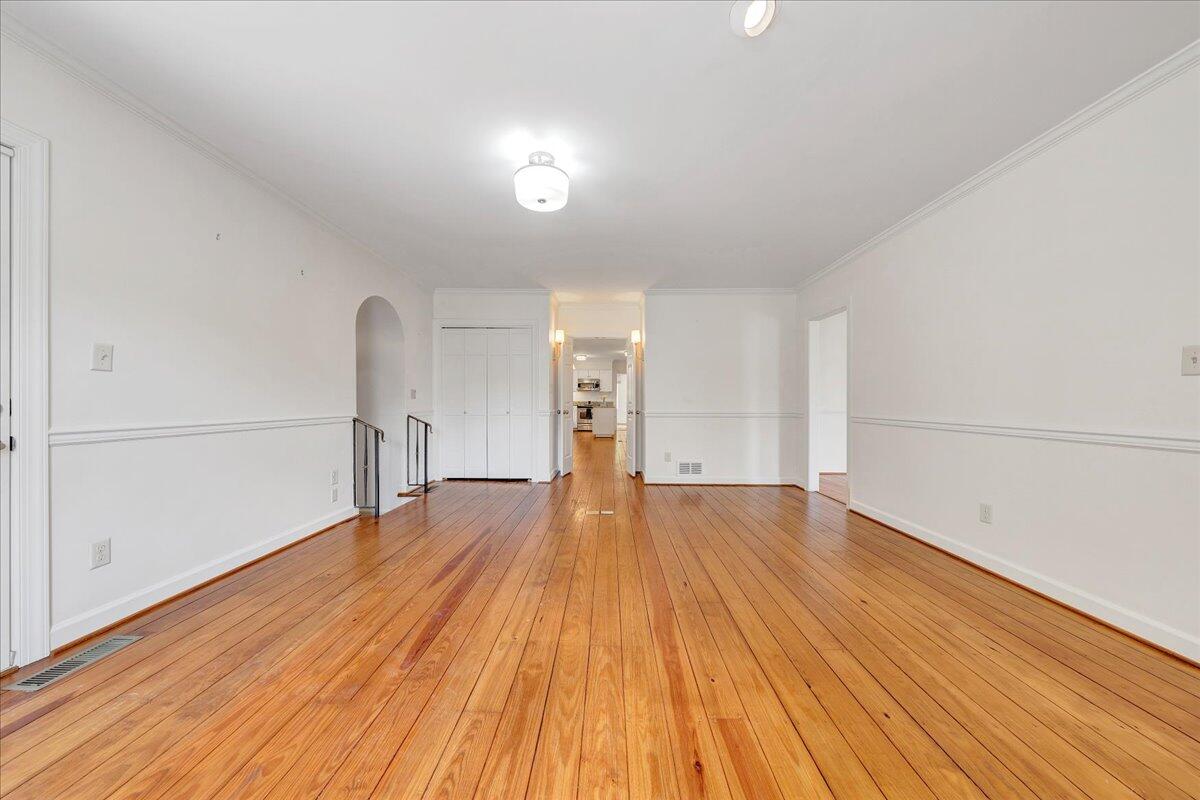 Empty room with polished hardwood floors and a view through to the kitchen