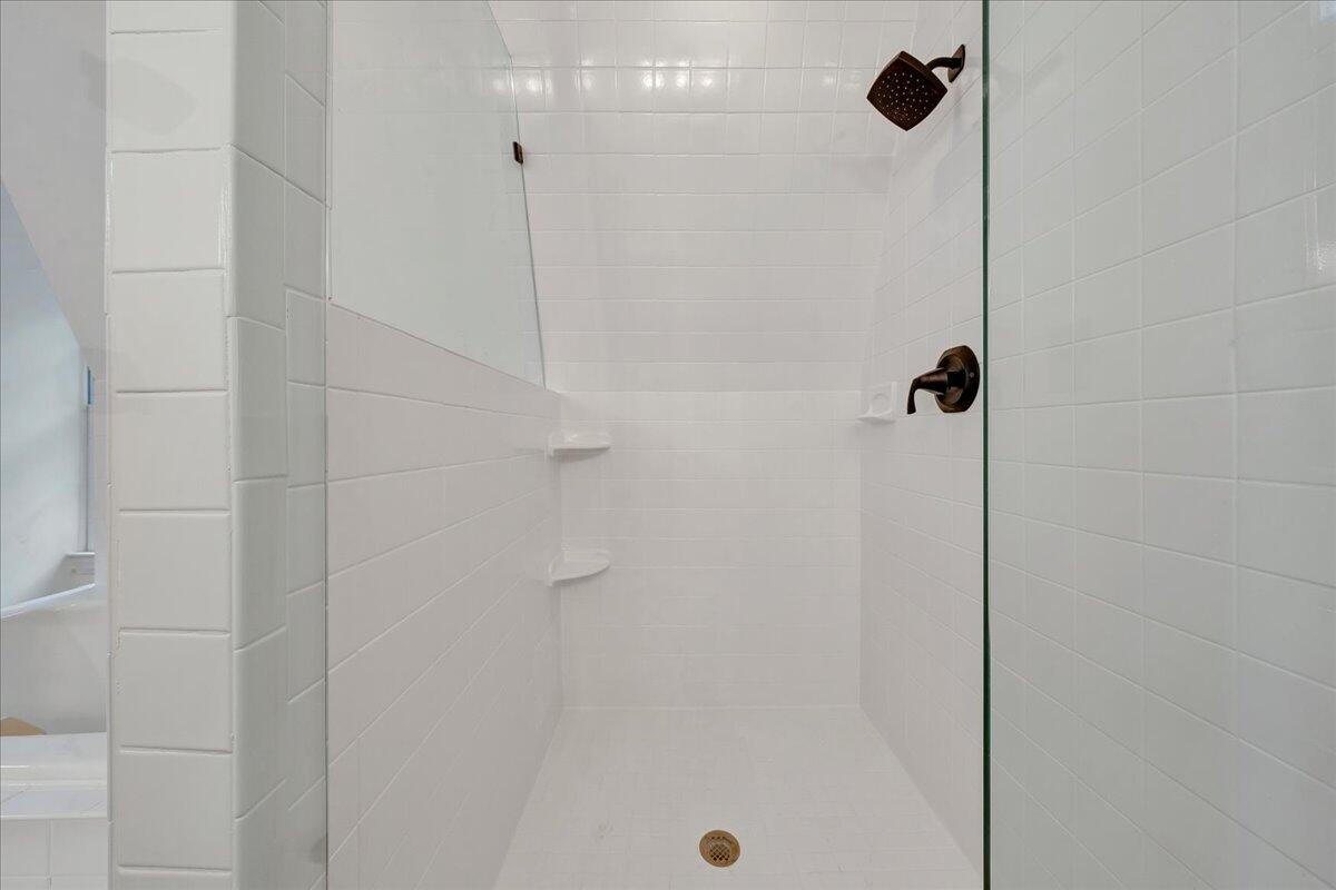 White tiled walk-in shower with glass panel, dark bronze fixtures, and built-in corner shelves.