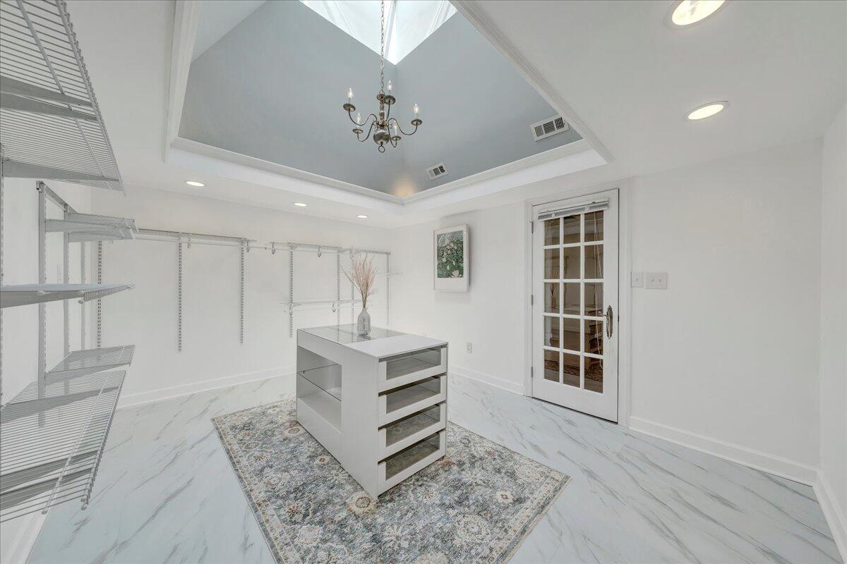 Walk-in closet with wire shelving, a central drawer island, marble-look floors, and a tray ceiling.