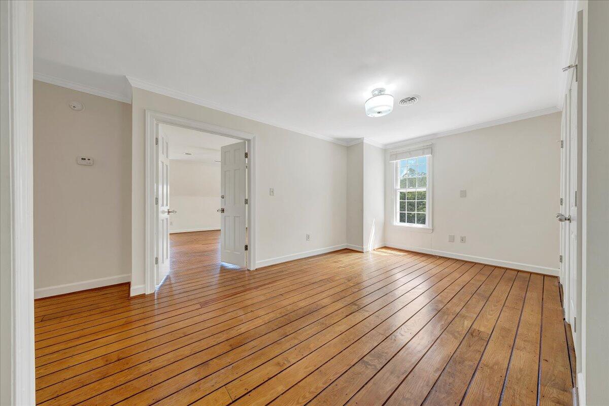 Empty bedroom with polished hardwood floors, white trim, and a sunlit window.