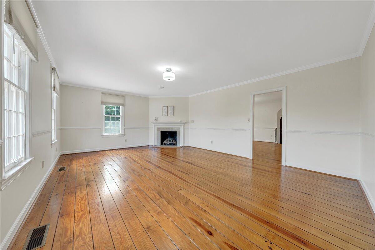 Vacant living room with polished hardwood floors, large windows, and a fireplace.