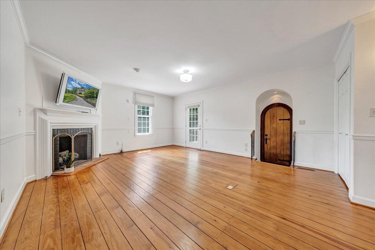 Empty living room with hardwood floors, a white fireplace, and an arched wooden entry door.