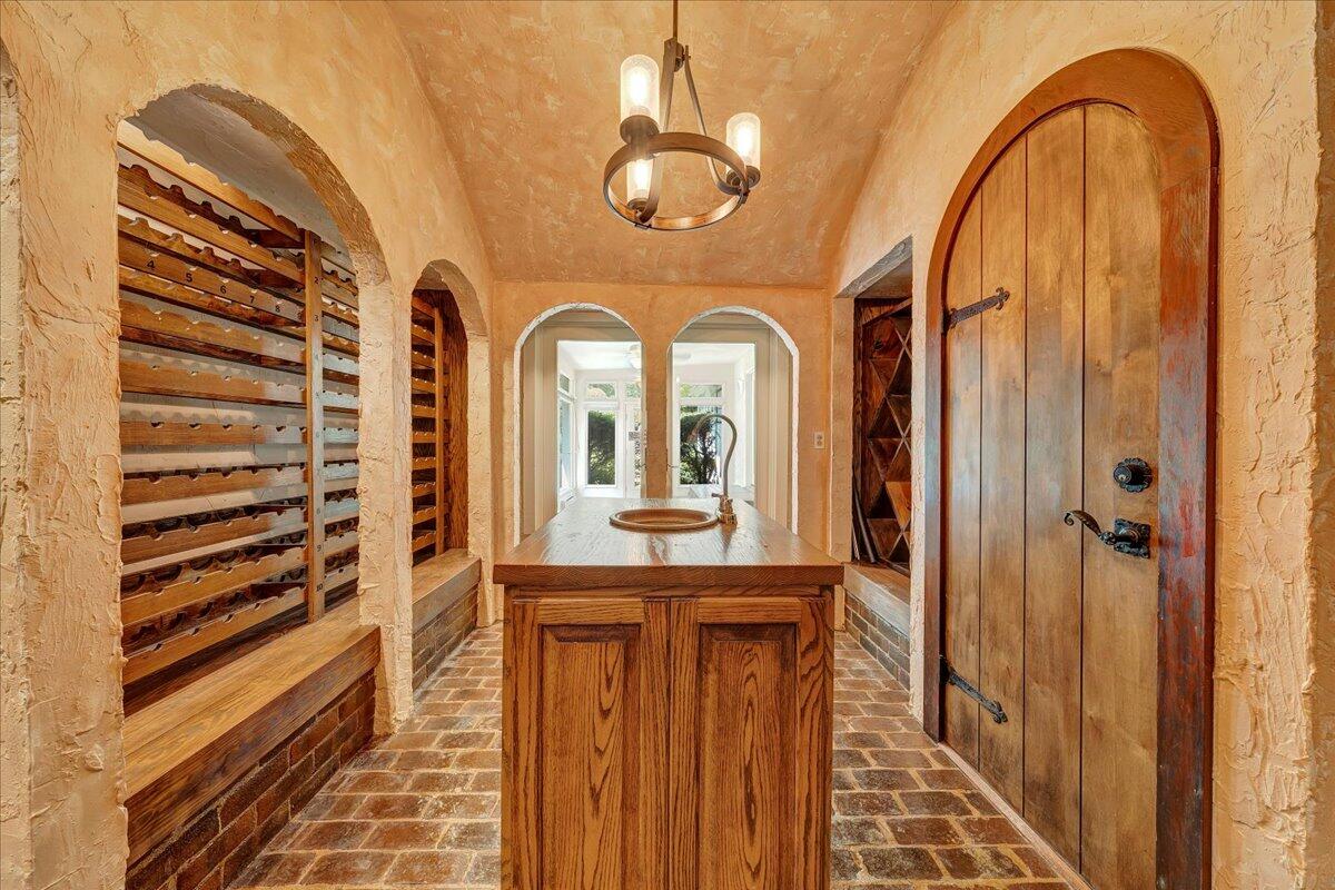 Wine cellar with built-in bottle racks, brick flooring, a wood island, and an arched wooden door.