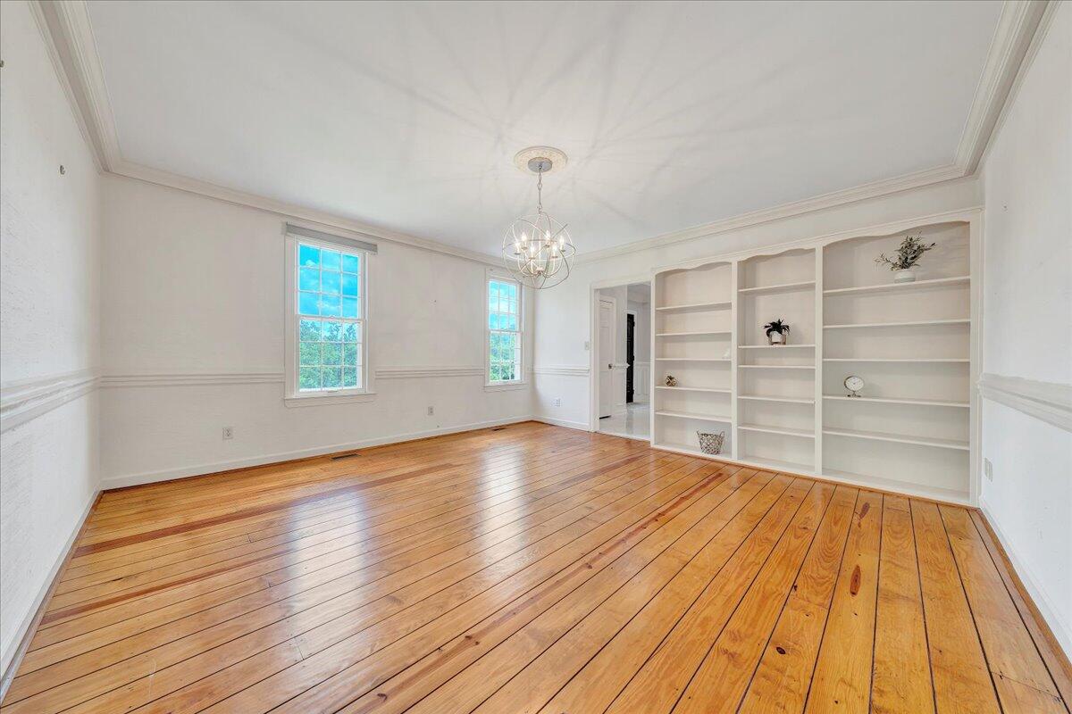 Empty room with polished hardwood floors, built-in white shelving, and a chandelier.