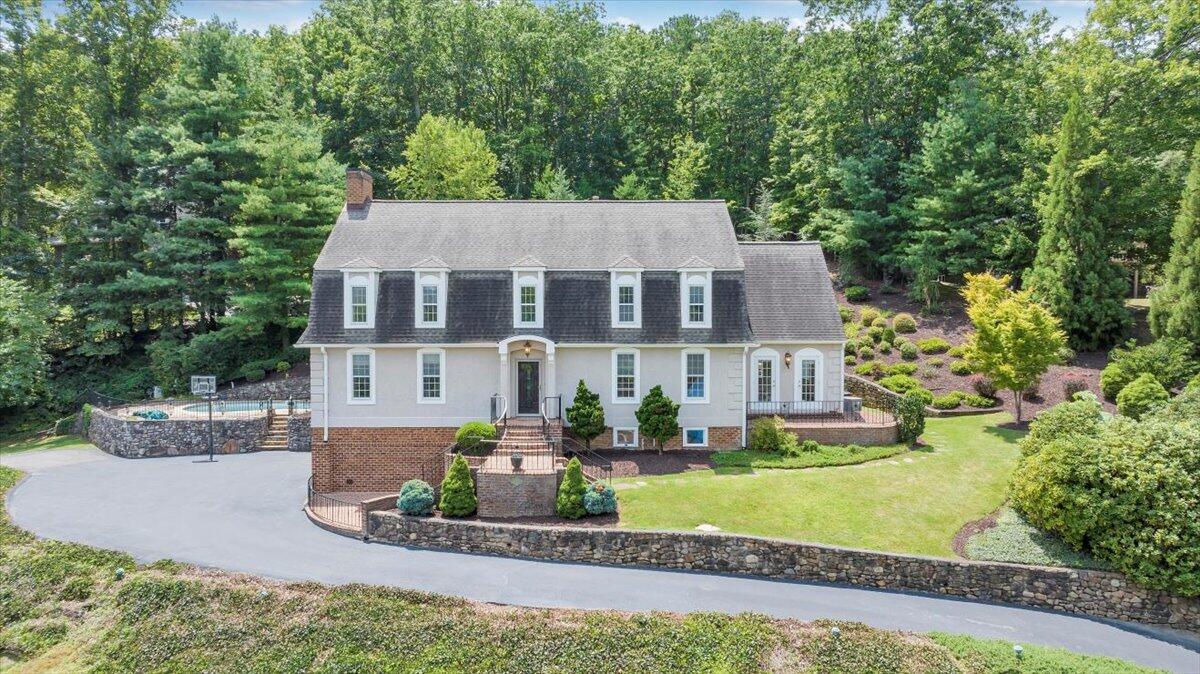 Home with white siding, brick lower level, dormer windows, and a fenced pool beside the driveway.