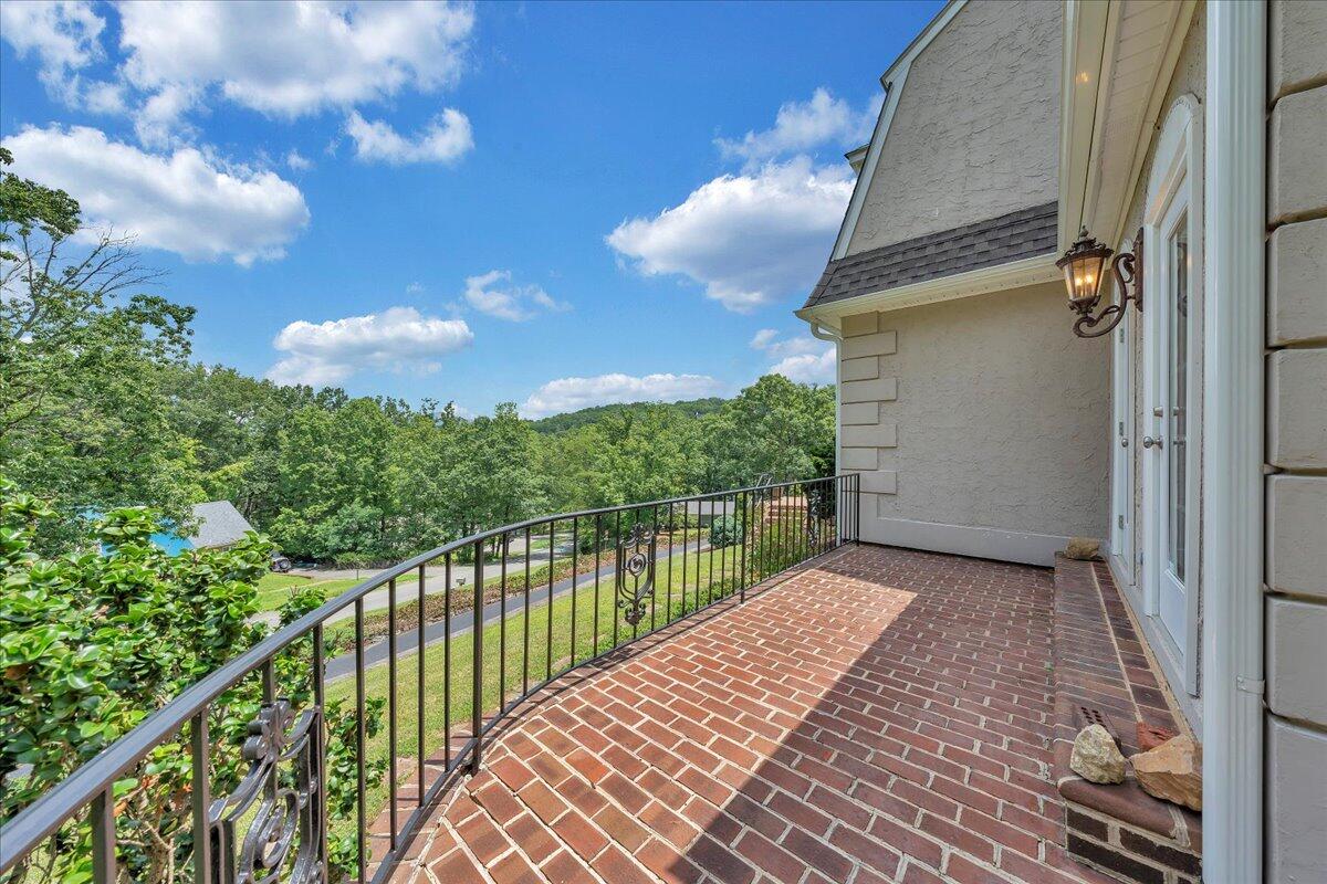 Brick balcony with a black metal railing overlooking wooded hills.