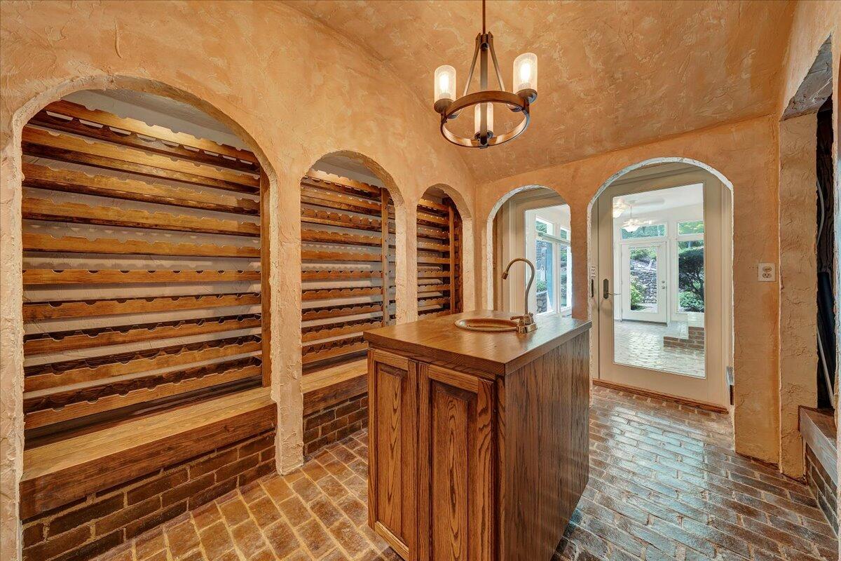 Wine cellar with arched wooden wine racks, a central island sink, and brick flooring.