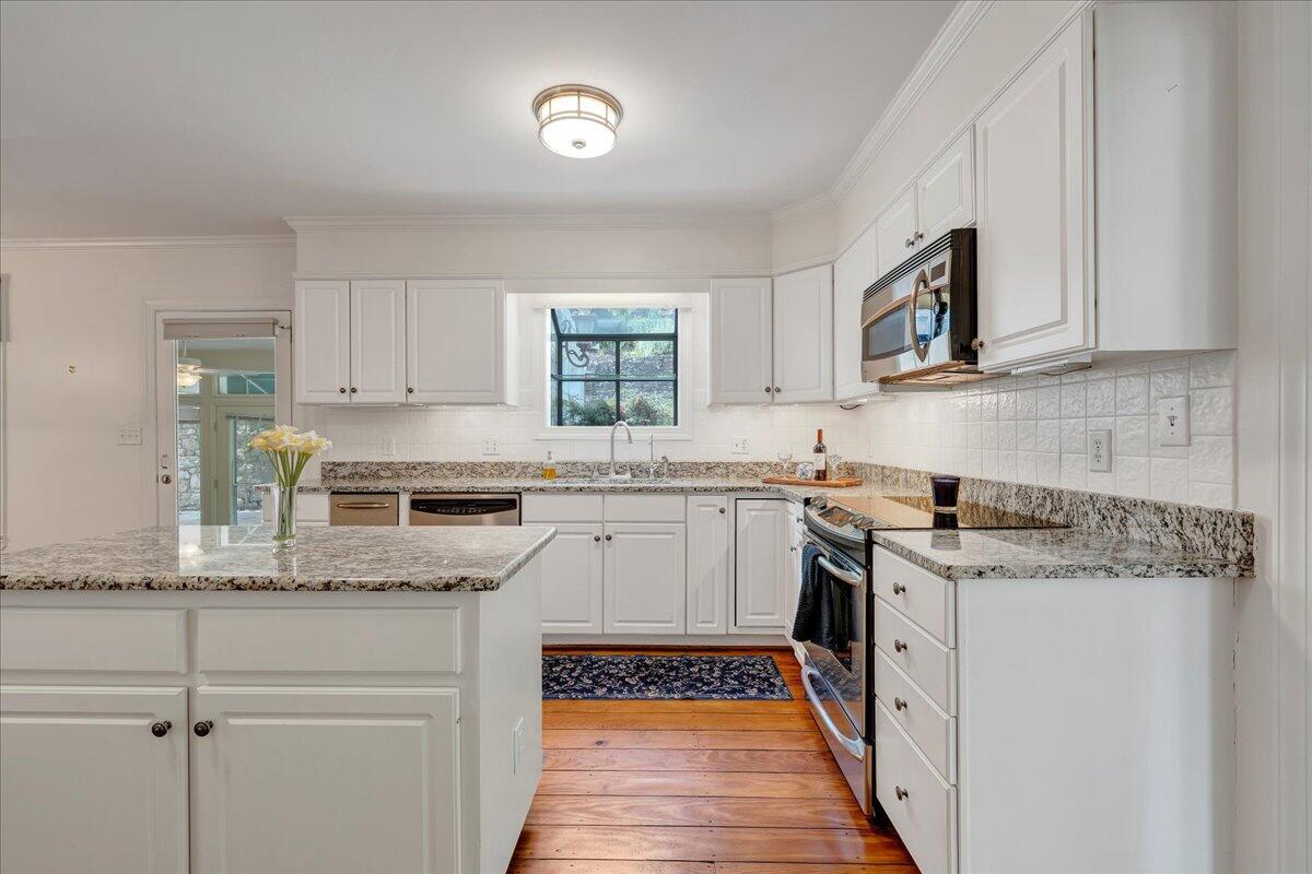 Bright kitchen with white cabinets, granite counters, stainless steel appliances, and wide-plank wood floors.