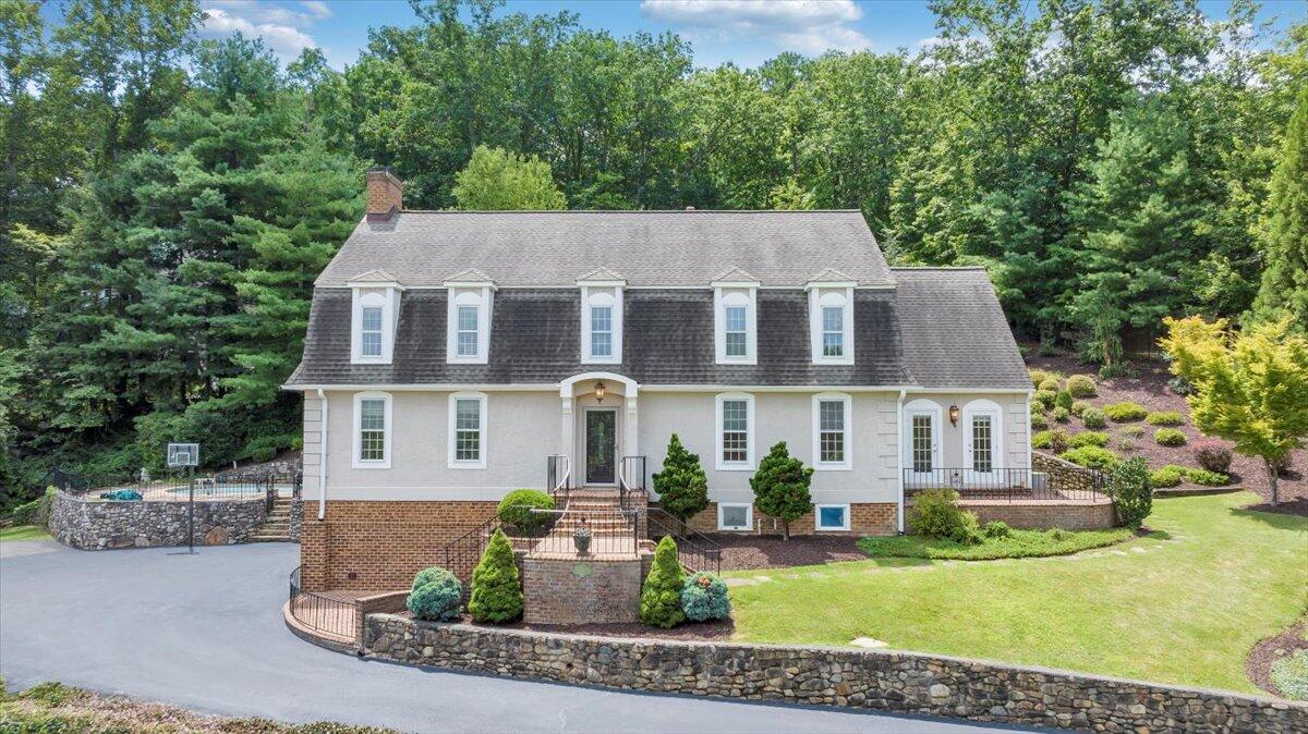 Two-story home with white siding, brick lower level, and landscaped grounds beneath mature trees.