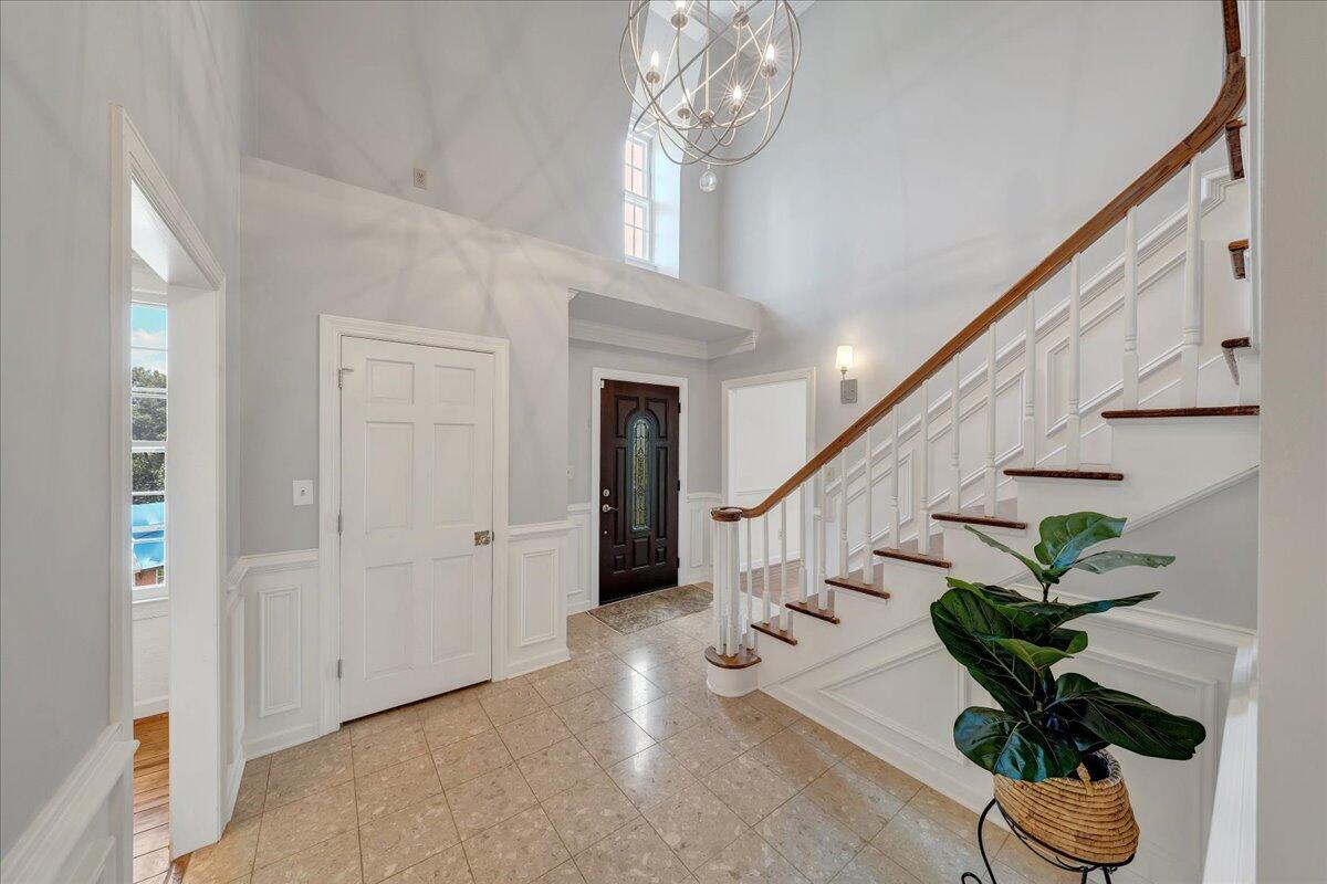 Two-story foyer with a sweeping staircase, dark front door, tiled floor, and modern chandelier.