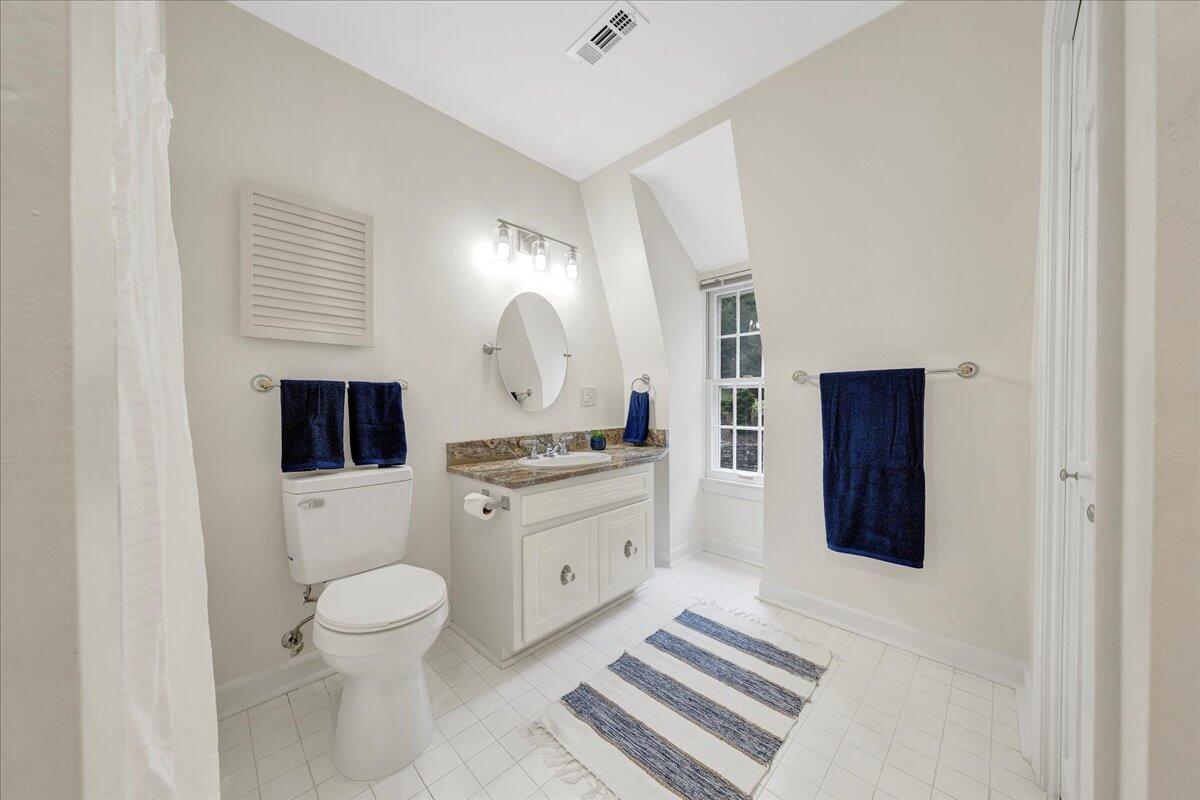 Bright bathroom with a white vanity, toilet, tiled floor, and window.