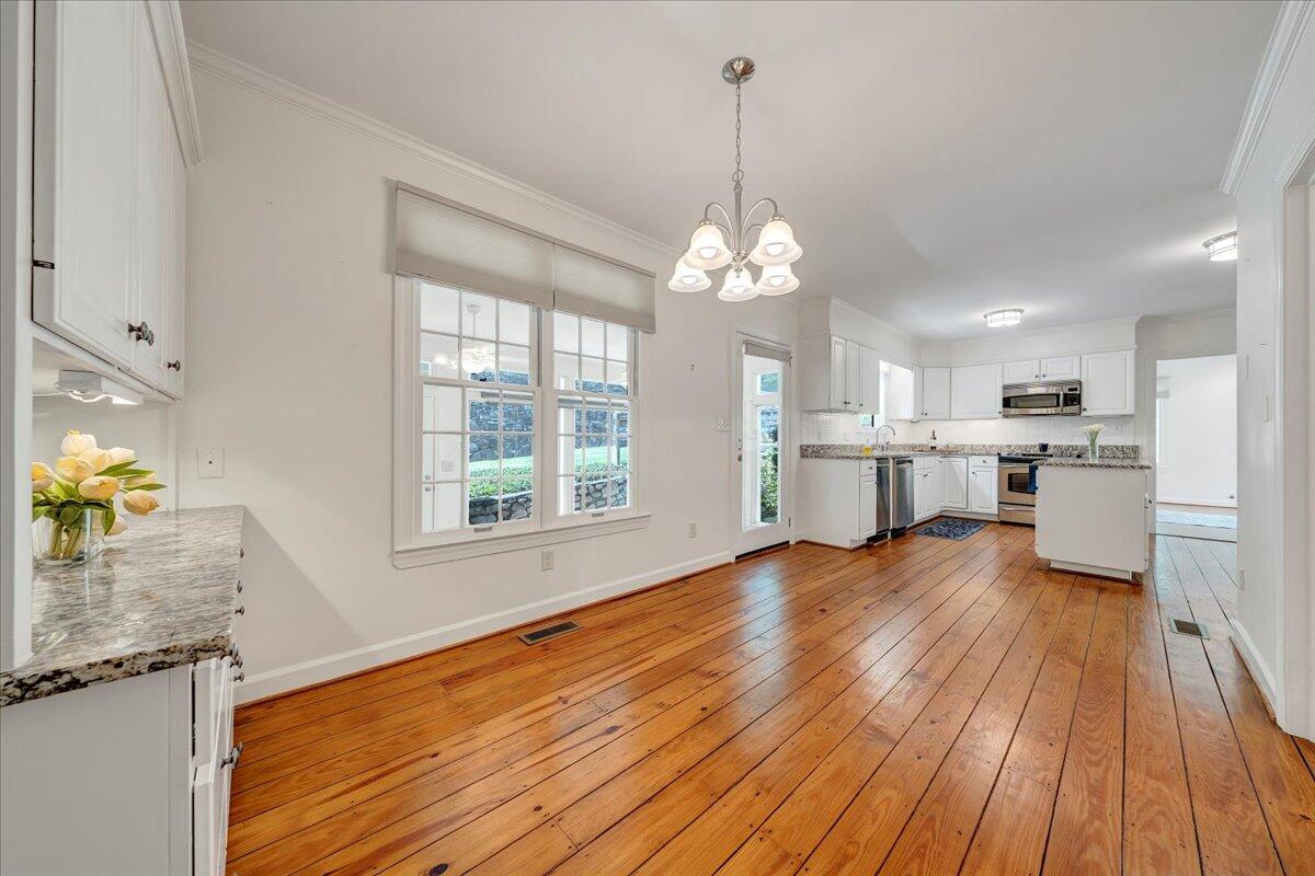 Bright white kitchen with a center island, granite counters, stainless appliances, and wide-plank hardwood floors.