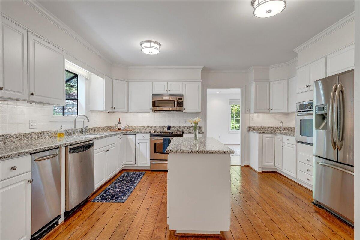 Kitchen with white cabinetry, stainless steel appliances, a central island, and warm wood floors.