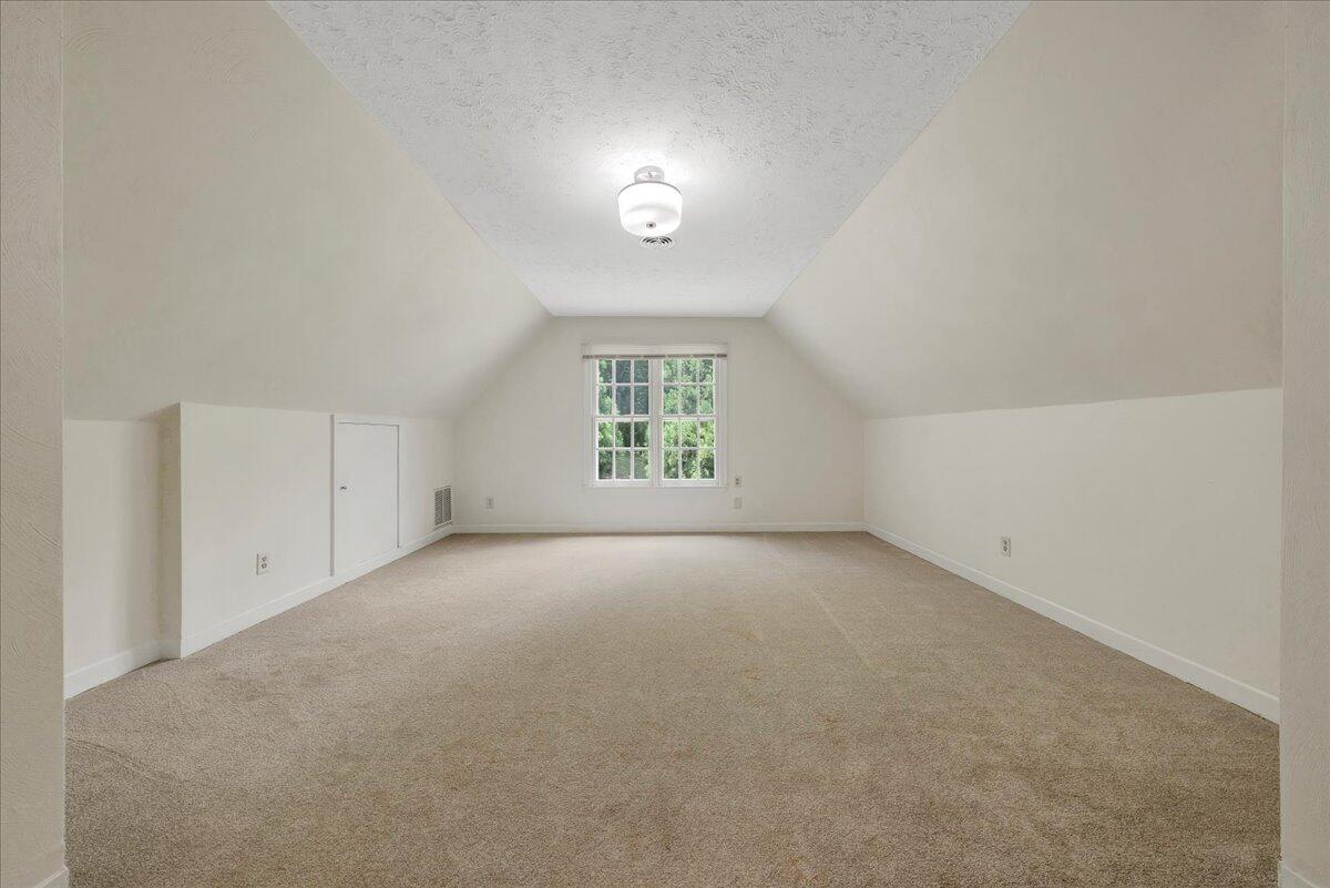 Empty carpeted upper-floor room with sloped ceilings and a multipane window.